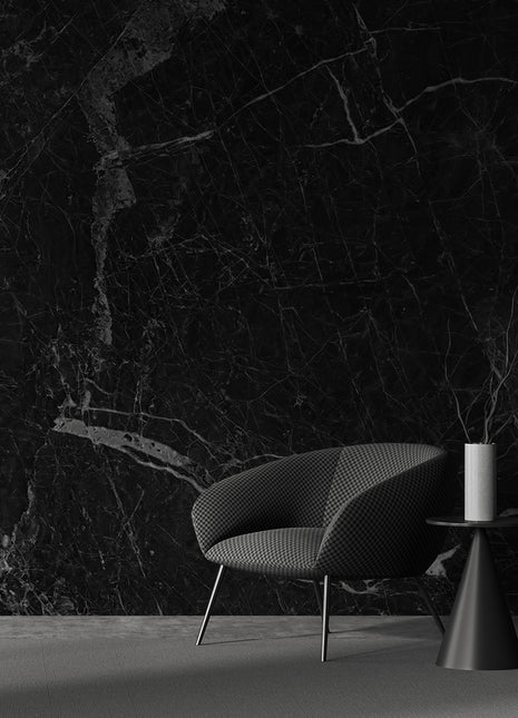 A modern living room with a black marble wall featuring a contemporary chair and a cylindrical table with a white lamp.